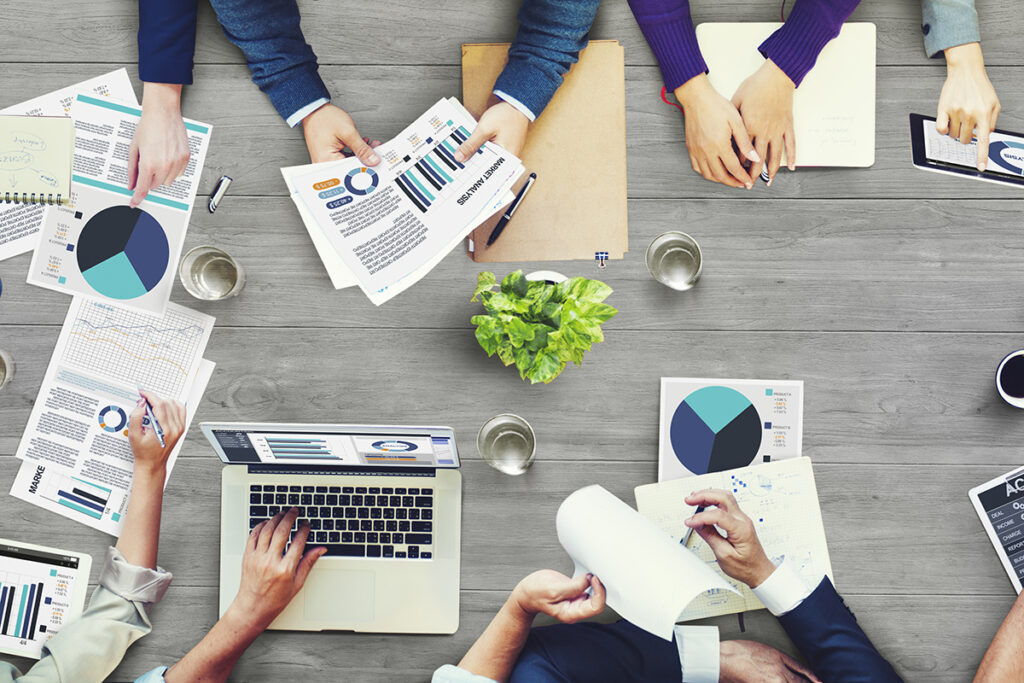 a group of people sitting around a table with laptops and papers