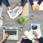 a group of people sitting around a table with laptops and papers